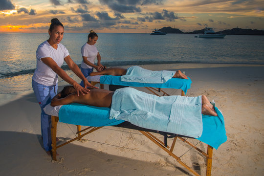 Women giving massage therapy stretch head neck outdoor at Caribbean beach to a couple on the massage table portable to relax. Caribbean turquoise water and sunset beach background .