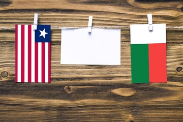 Hanging flags of Liberia and Madagascar attached to rope with clothes pins with copy space on white note paper on wooden background.Diplomatic relations between countries.