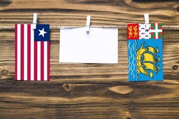 Hanging flags of Liberia and Saint Pierre And Miquelon attached to rope with clothes pins with copy space on white note paper on wooden background.Diplomatic relations between countries.