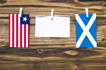 Hanging flags of Liberia and Scotland attached to rope with clothes pins with copy space on white...