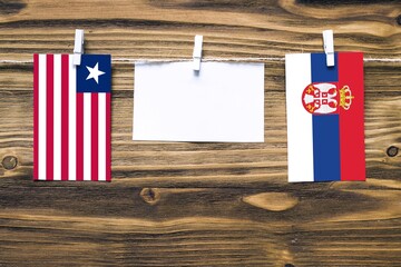 Hanging flags of Liberia and Serbia attached to rope with clothes pins with copy space on white...