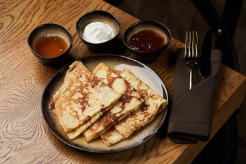 Homemade pancakes with jam, honey and sour cream bowls, close-up