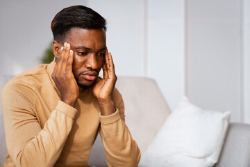 Man Having Migraine Massaging Temples Sitting On Sofa At Home