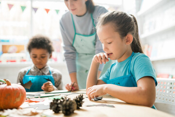 Cute pensive schoolgirl looking at small black paper bat on desk at lesson