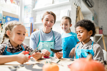 Multicultural youthful schoolkids and teacher looking at handmade decoration