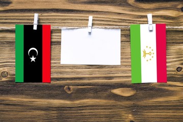 Hanging flags of Libya and Tajikistan attached to rope with clothes pins with copy space on white...
