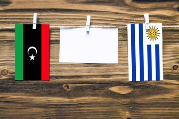 Hanging flags of Libya and Uruguay attached to rope with clothes pins with copy space on white note...
