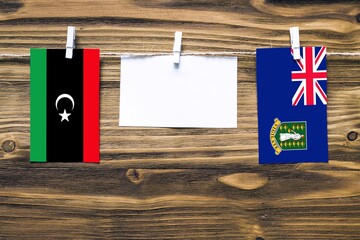 Hanging flags of Libya and British Virgin Islands attached to rope with clothes pins with copy space on white note paper on wooden background.Diplomatic relations between countries.