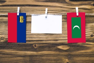 Hanging flags of Liechtenstein and Maldives attached to rope with clothes pins with copy space on white note paper on wooden background.Diplomatic relations between countries.