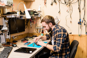 Professional repairman bending over demounted smartphone and fixing tiny details