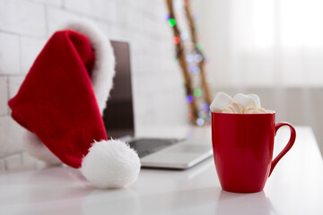 Obraz na płótnie Canvas Laptop with Santa's hat and cup of cocoa with marshmallows