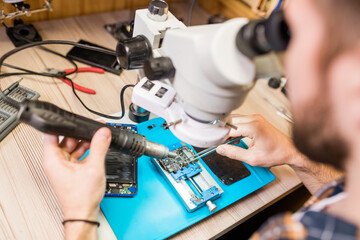 Hands of repairman with electric handtool looking in microscope during work