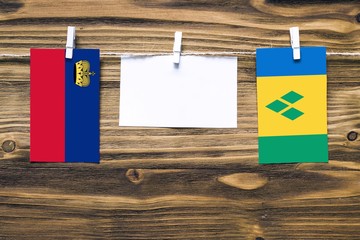 Hanging flags of Liechtenstein and Saint Vincent And The Grenadines attached to rope with clothes pins with copy space on white note paper on wooden background.Diplomatic relations between countries.