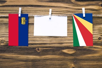 Hanging flags of Liechtenstein and Seychelles attached to rope with clothes pins with copy space on white note paper on wooden background.Diplomatic relations between countries.
