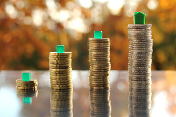 coins stacked with models of houses, EU cash on a blurred background autumn landscape in the back light, the concept of housing, credit, mortgages