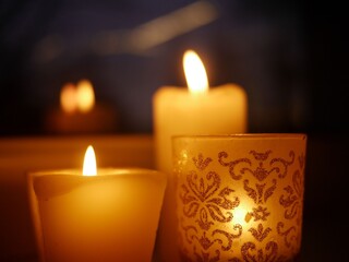 Closeup photo of three lit candles - two paraffin wax candles and one tealight in a glass candle...