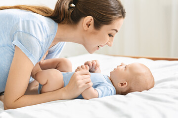 Fototapeta na wymiar Young mother playing with her cute newborn baby in bed