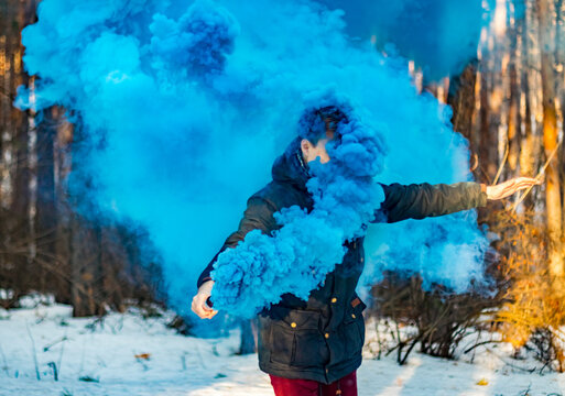 Young man posing with a blue smoke bomb in a winter parka on a winter day. - Powered by Adobe