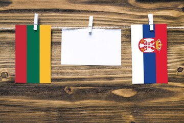 Hanging flags of Lithuania and Serbia attached to rope with clothes pins with copy space on white...