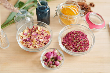 Group of bowls with dry rose petals and small jar with orange slices on table