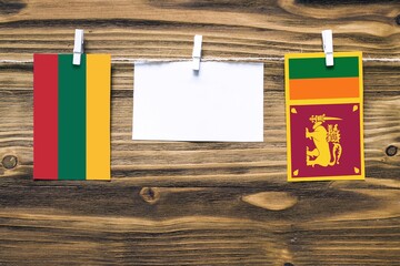 Hanging flags of Lithuania and Sri Lanka attached to rope with clothes pins with copy space on white note paper on wooden background.Diplomatic relations between countries.