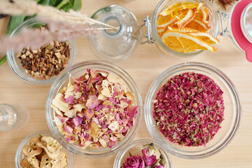 Overview of bowls with dry rose petals, pear and orange slices on wooden table