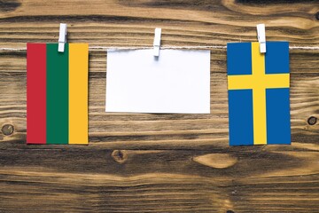 Hanging flags of Lithuania and Sweden attached to rope with clothes pins with copy space on white note paper on wooden background.Diplomatic relations between countries.