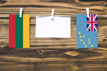 Hanging flags of Lithuania and Tuvalu attached to rope with clothes pins with copy space on white note paper on wooden background.Diplomatic relations between countries.