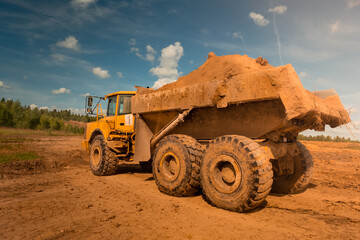 large yellow dirty dump truck with large wheels loaded with earth