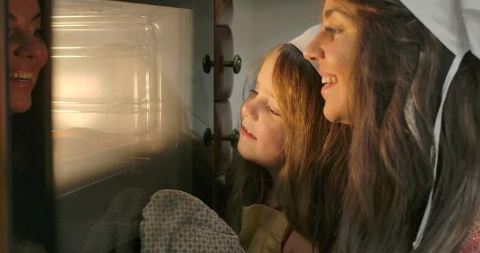 Close-up faces of little Caucasian brunette girl and her mother looking into oven. Happy smiling family baking at the kitchen at home. Cinema 4k footage ProRes HQ.