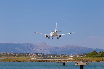 Fototapeta na wymiar Passenger's airplane is landing at Kerkyra Airport. Greece, Corfu island. Decrease in height, close-up. Runway on the background of mountains and sea.
