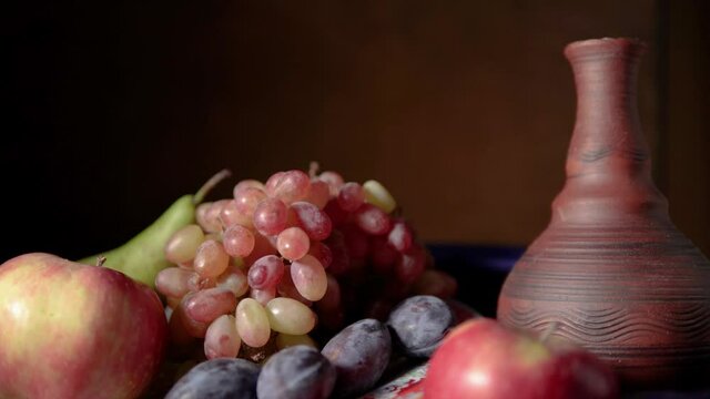Still life with fruit and red wine. Grapes, apples, pear, plums, nuts and blue drapery