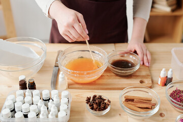 Craftswoman mixing liquid soap mass with orange essential oil in bowl