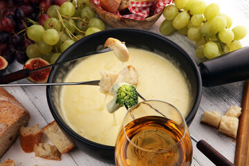 Gourmet Swiss fondue dinner on a winter evening with assorted cheeses on a board alongside a heated pot of cheese fondue with two forks dipping