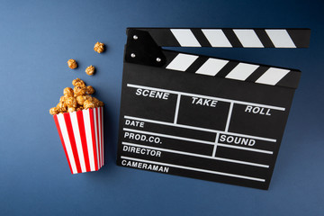 Cinema concept. Movie clapper and caramel popcorn on blue background.