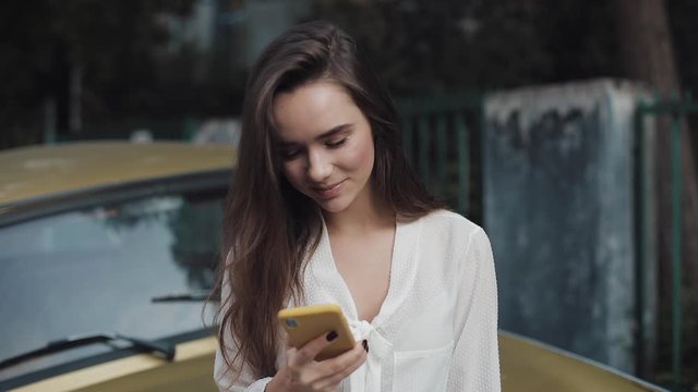 Young Brunette Smiling Beautiful Girl Ending Video Call via her Smart Phone, Waving Bye-Bye Outdoors. Young Girl Making and Sending Video Message while Standing Outdoors.