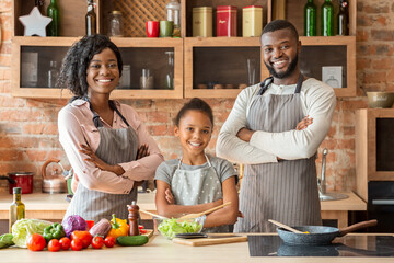 Successful family in aprons posing over kitchen background