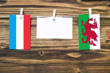Hanging flags of Luxembourg and Wales attached to rope with clothes pins with copy space on white...