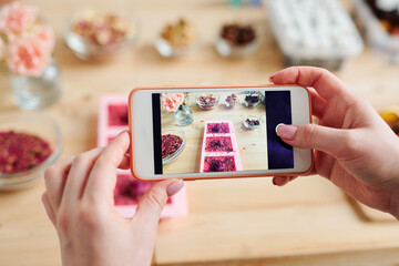 Hands of girl holding smartphone over table while taking photo of handmade soap