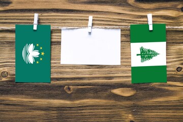 Hanging flags of Macao and Norfolk Island attached to rope with clothes pins with copy space on...