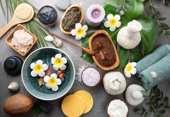 Fototapeta na wymiar Beautiful spa relax concept. Coffee with cinnamon scrub, green tea scrub, cotton pouches with herbs for massage, sea stones and other Spa accessories on grey table top view. Copy space.