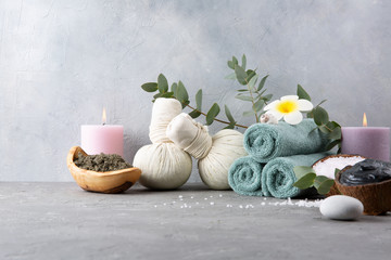 Beautiful spa and relax concept. Green tea scrub, dead sea mud, cotton pouches with herbs for massage, sea stones, eucalyptus and other Spa accessories on grey table.