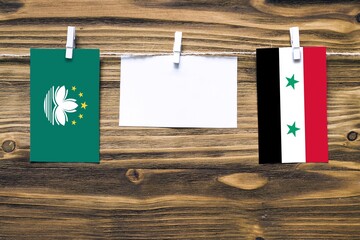 Hanging flags of Macao and Syria attached to rope with clothes pins with copy space on white note...