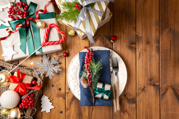 Christmas wooden table with served plate, gift boxes, decorations, toys and fir. Top view.