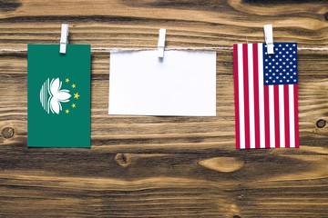 Hanging flags of Macao and United States attached to rope with clothes pins with copy space on white note paper on wooden background.Diplomatic relations between countries.
