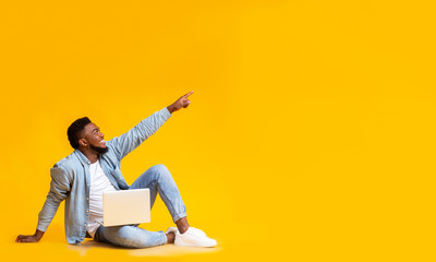African man sitting with laptop and pointing at copy space
