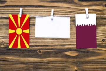 Hanging flags of Macedonia and Qatar attached to rope with clothes pins with copy space on white...