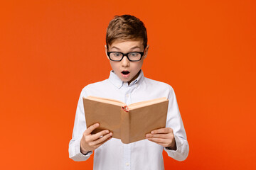 Amazed teen nerd in glasses emotionally reading book