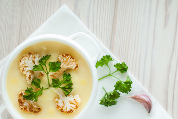 Homemade cauliflower and potato soup with a parsley and spice in the white bowl. top view