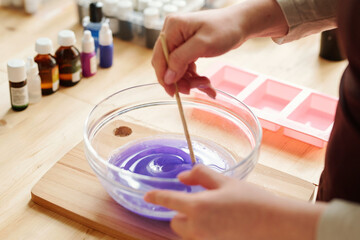 Fototapeta na wymiar Hands of creative girl mixing lavender color with liquid soap mass in glassware
